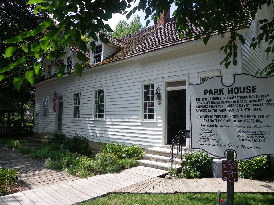 A white clapboard house with a shake roof framed by green leaves.