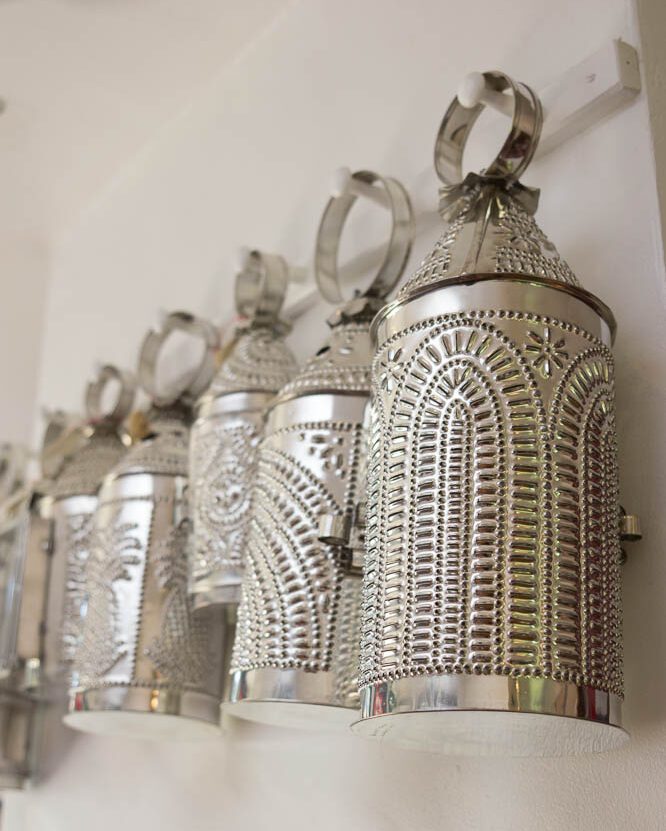 Several tin lanterns hanging in a row from pegs attached to a white wall.