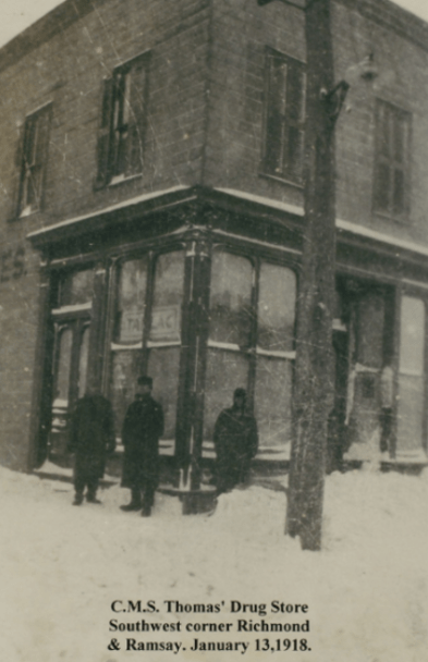 3 men standin in front of the corner of a two story Victorian shop